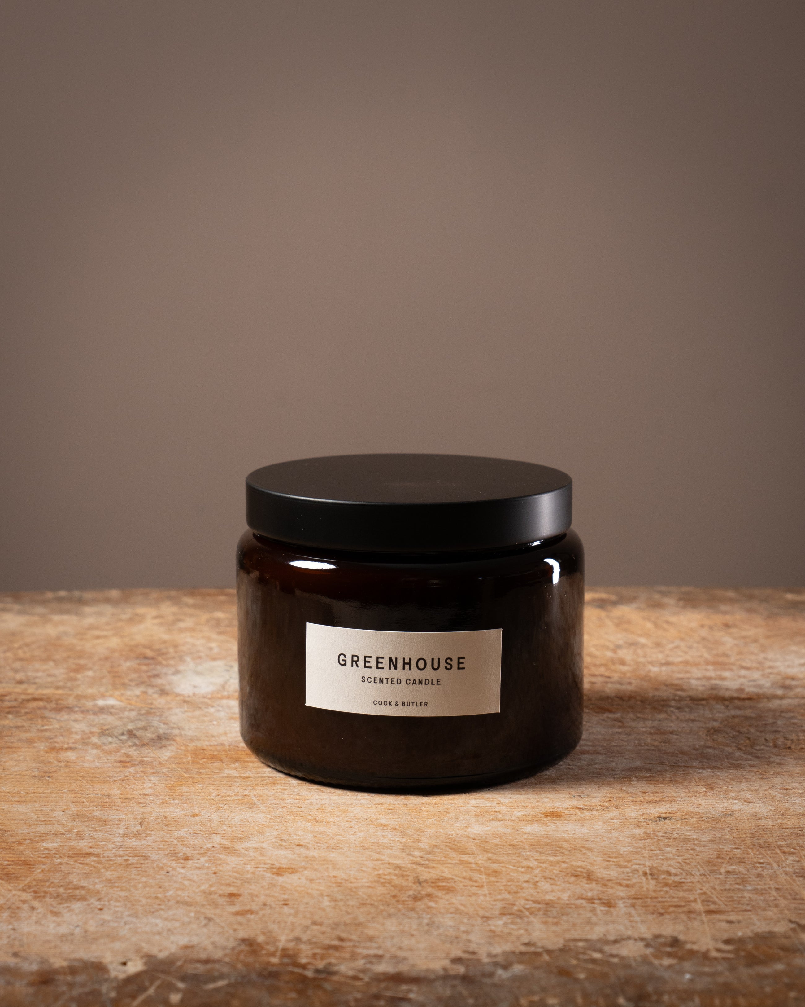 Cook and Butler scented candle on a wooden worktop with a label saying "greenhouse"