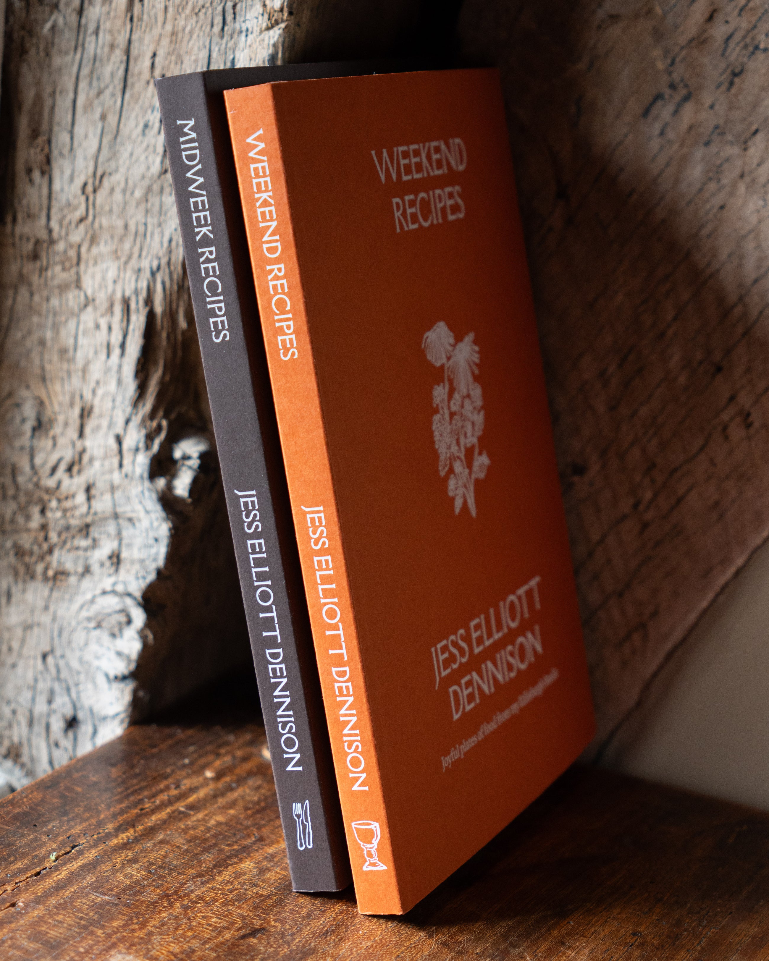 Two recipe books titled 'Weekend Recipes' and 'Midweek Recipes' by Jess Elliott Dennison on a wooden surface.