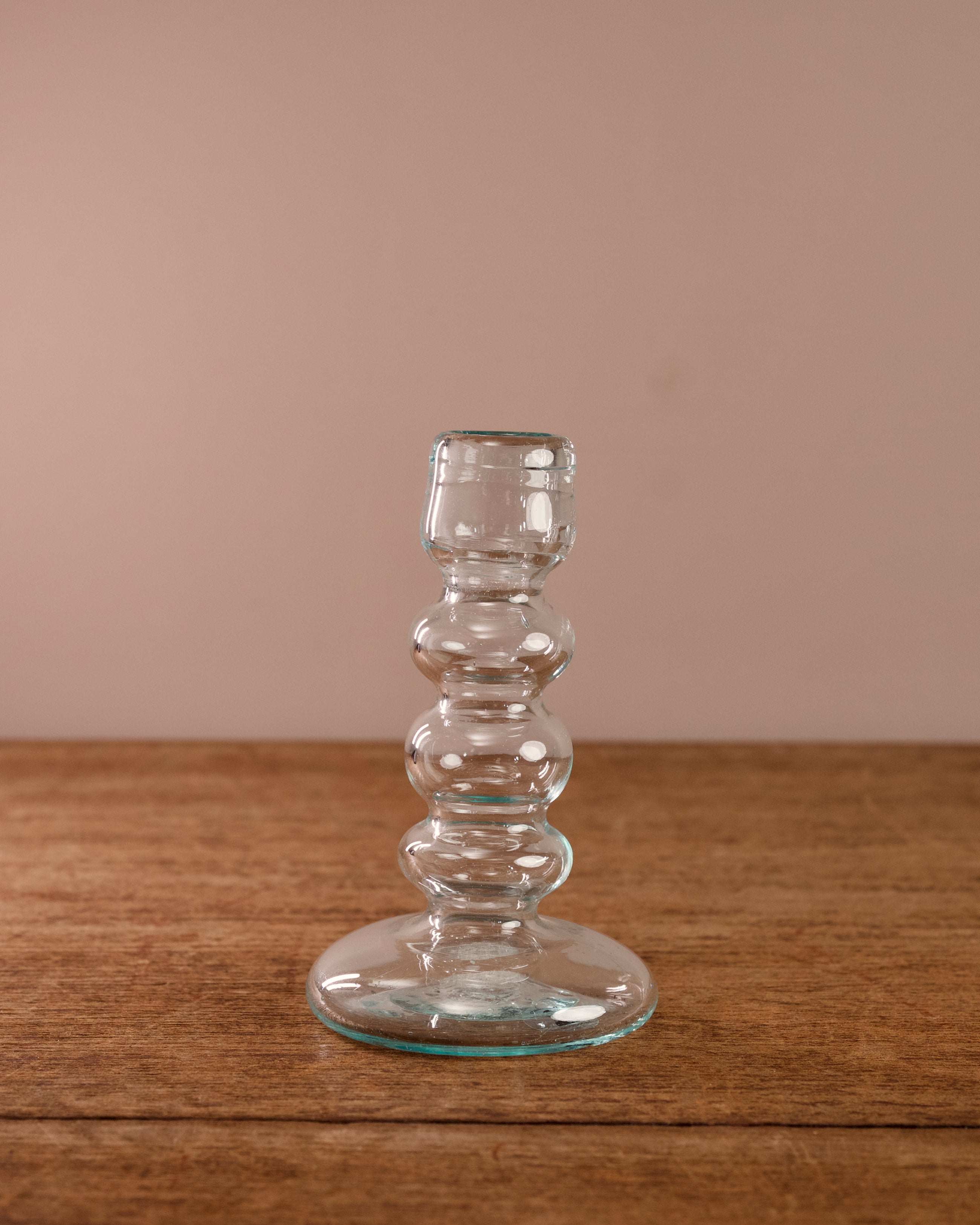 Clear glass candle holder on a wooden surface with a beige background