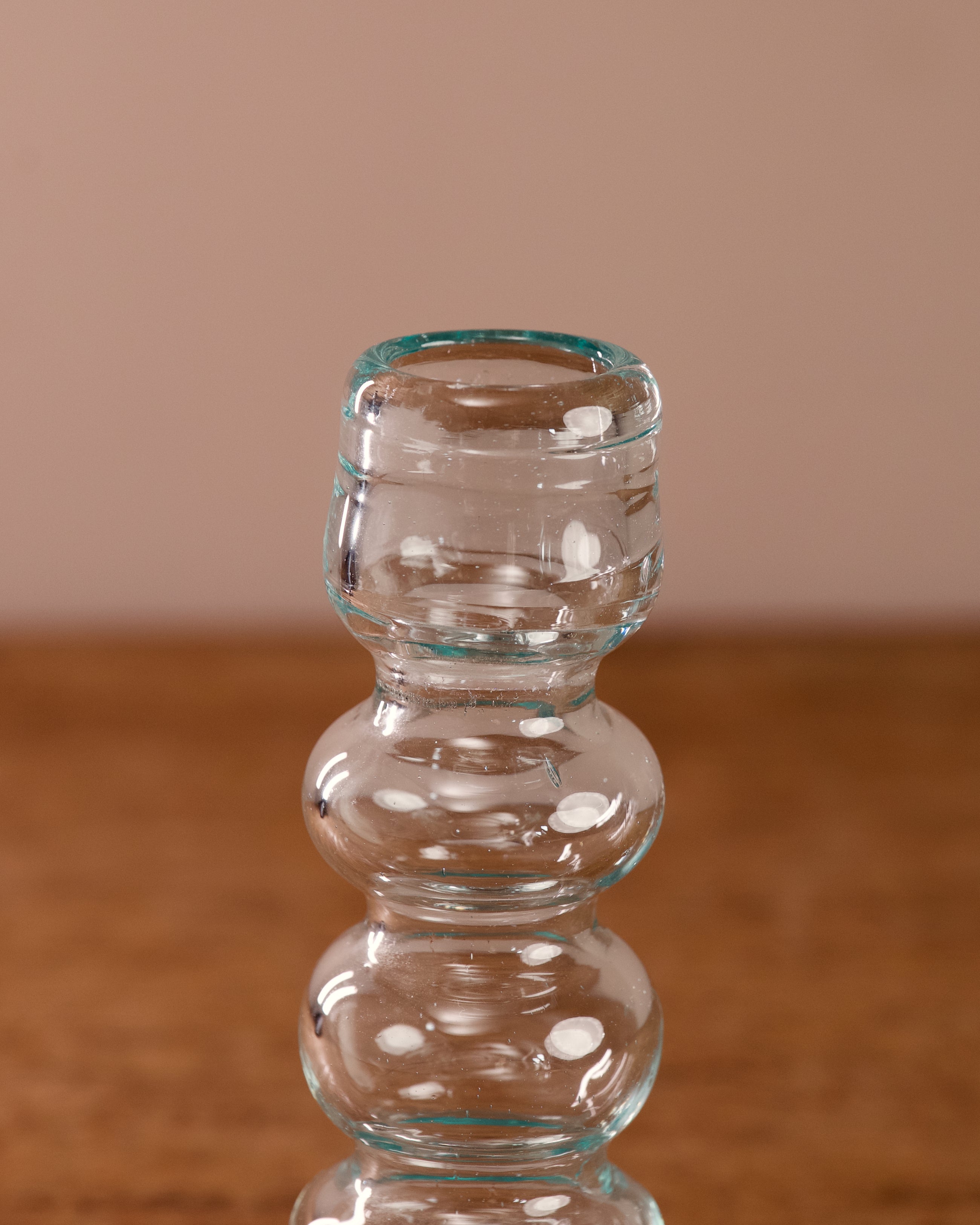 Clear glass candle holder on a wooden surface with a beige background