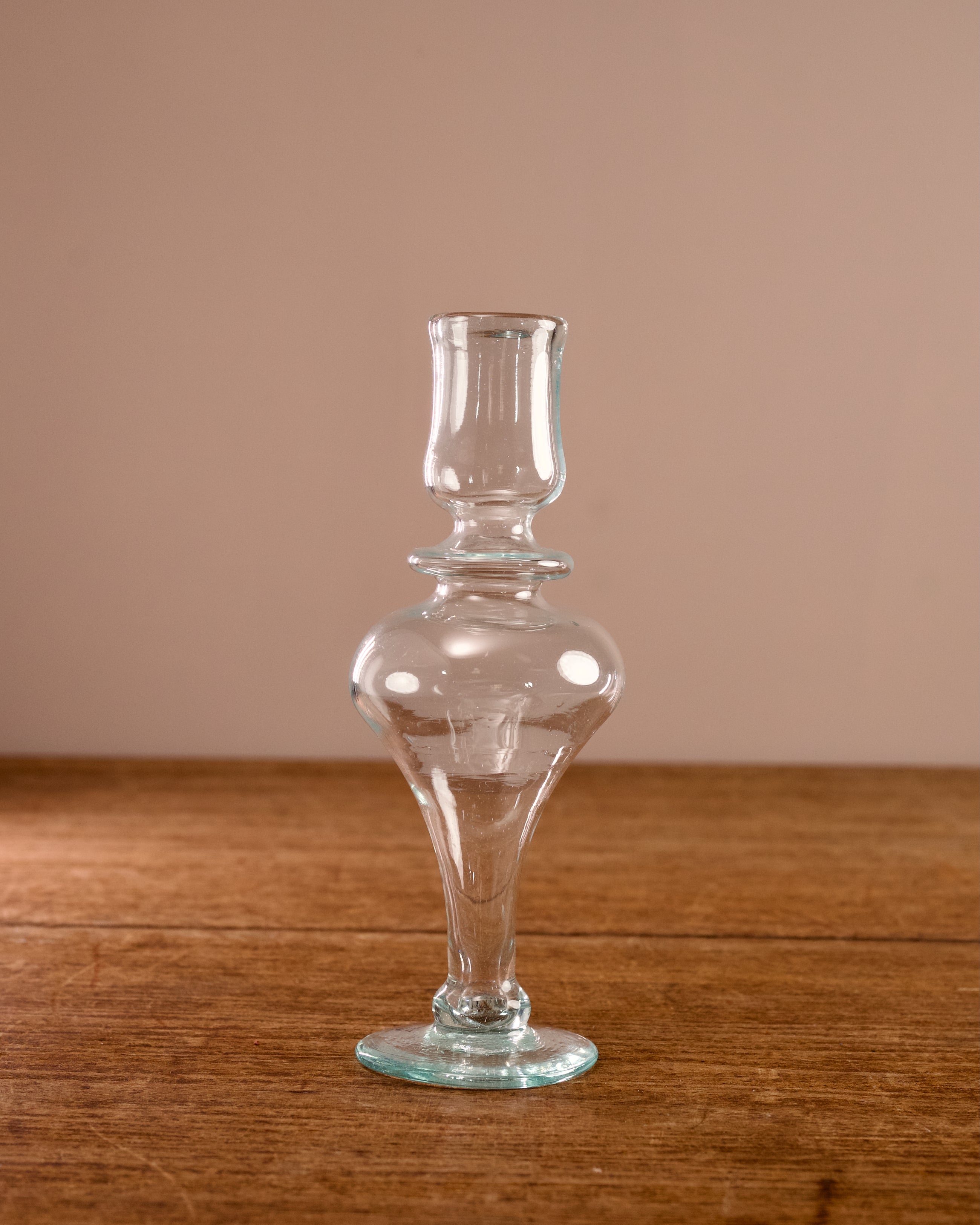 Clear glass candlestick on a wooden surface with a beige background