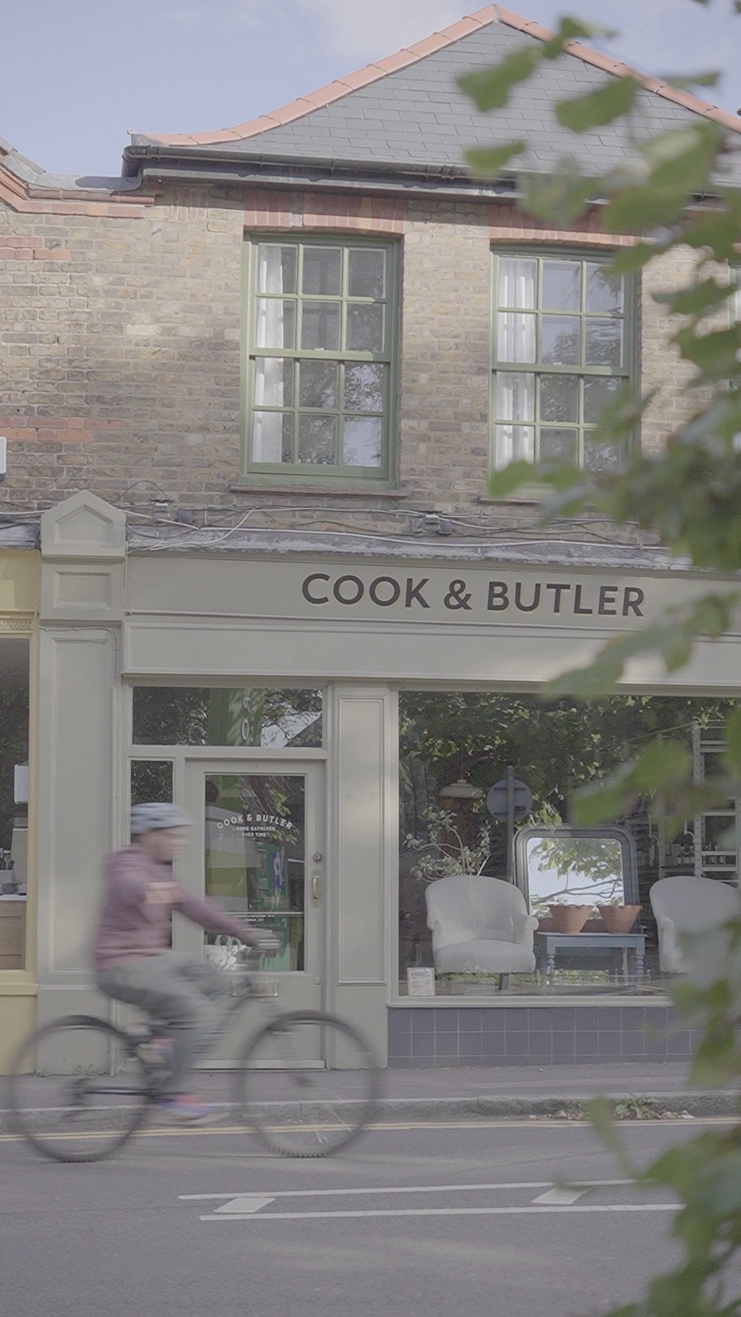 Storefront with 'Cook & Butler' sign, person on a bicycle passing by