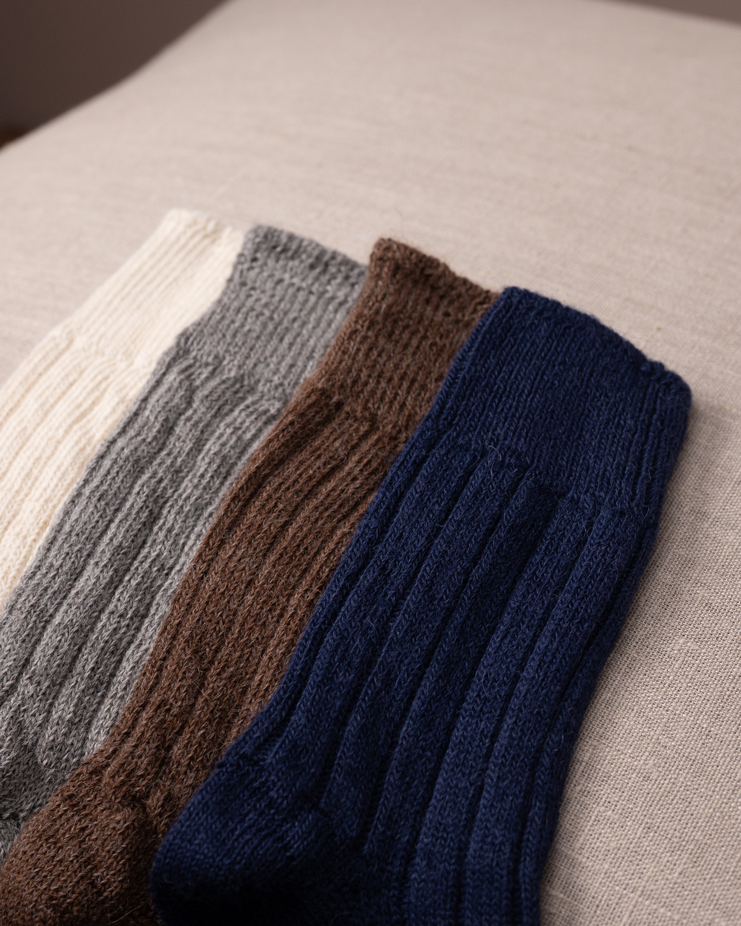 Four pairs of knitted socks in different colours on a textured surface.