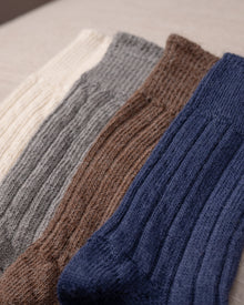 Four pairs of knitted socks in white, grey, brown, and blue on a light background.