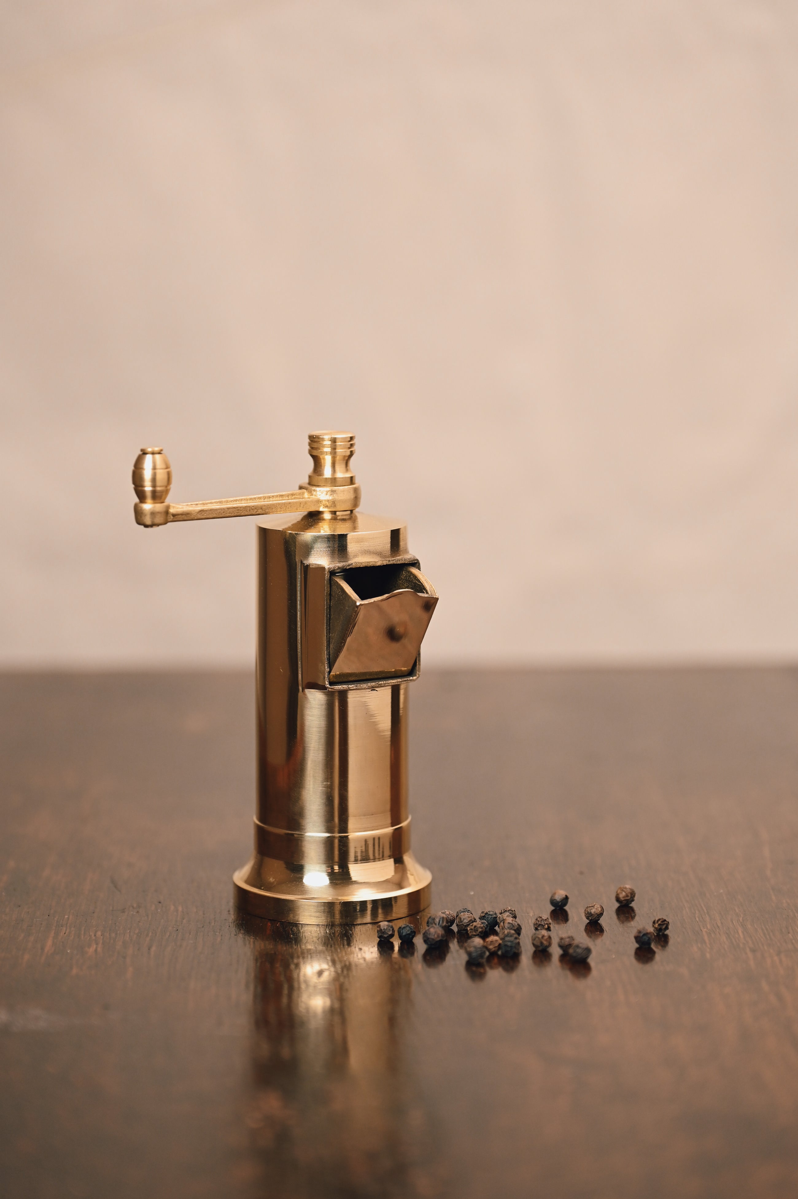 Brass pepper grinder with peppercorns on a wooden surface