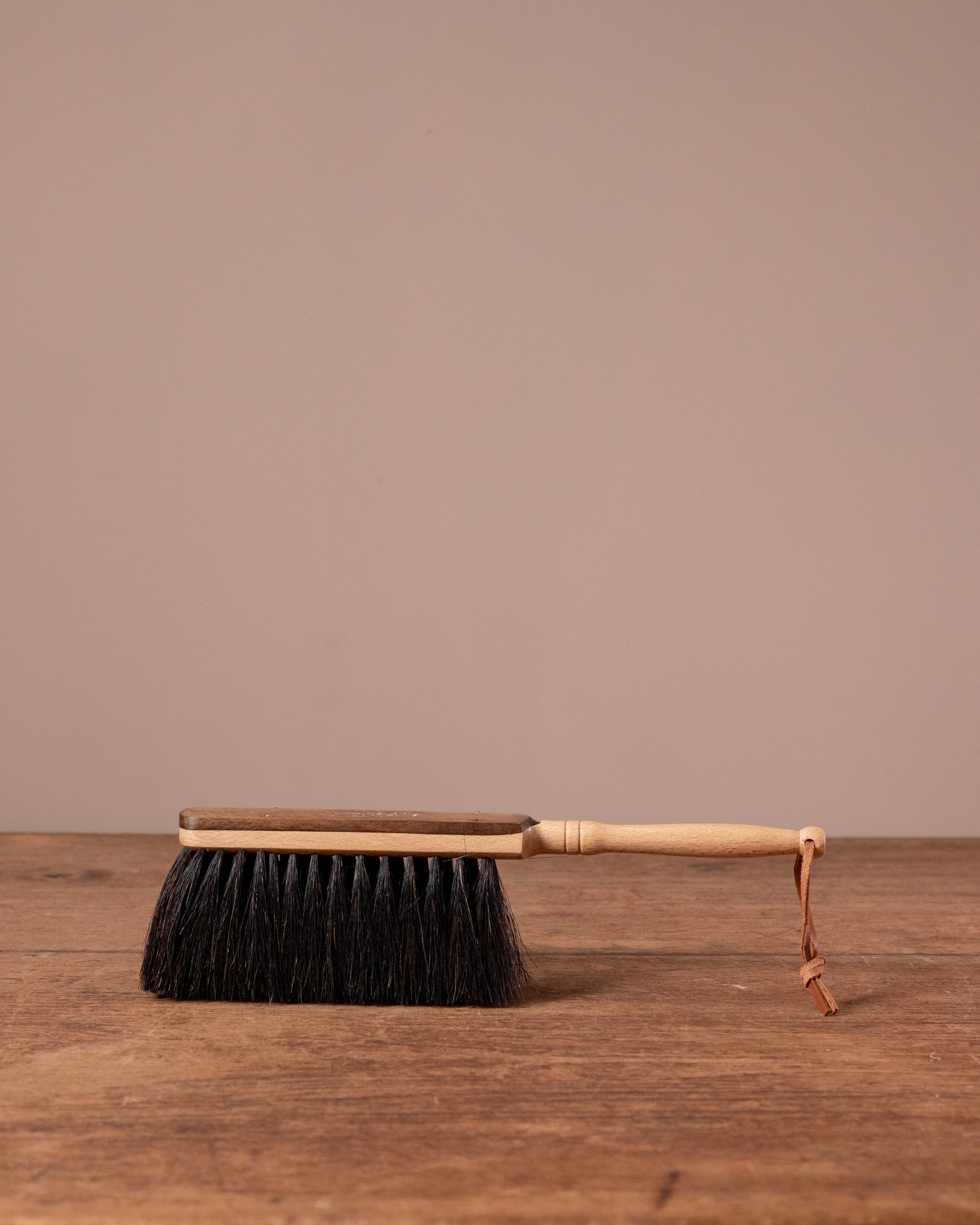 Traditional dustpan with bristles on a wooden surface against a beige background