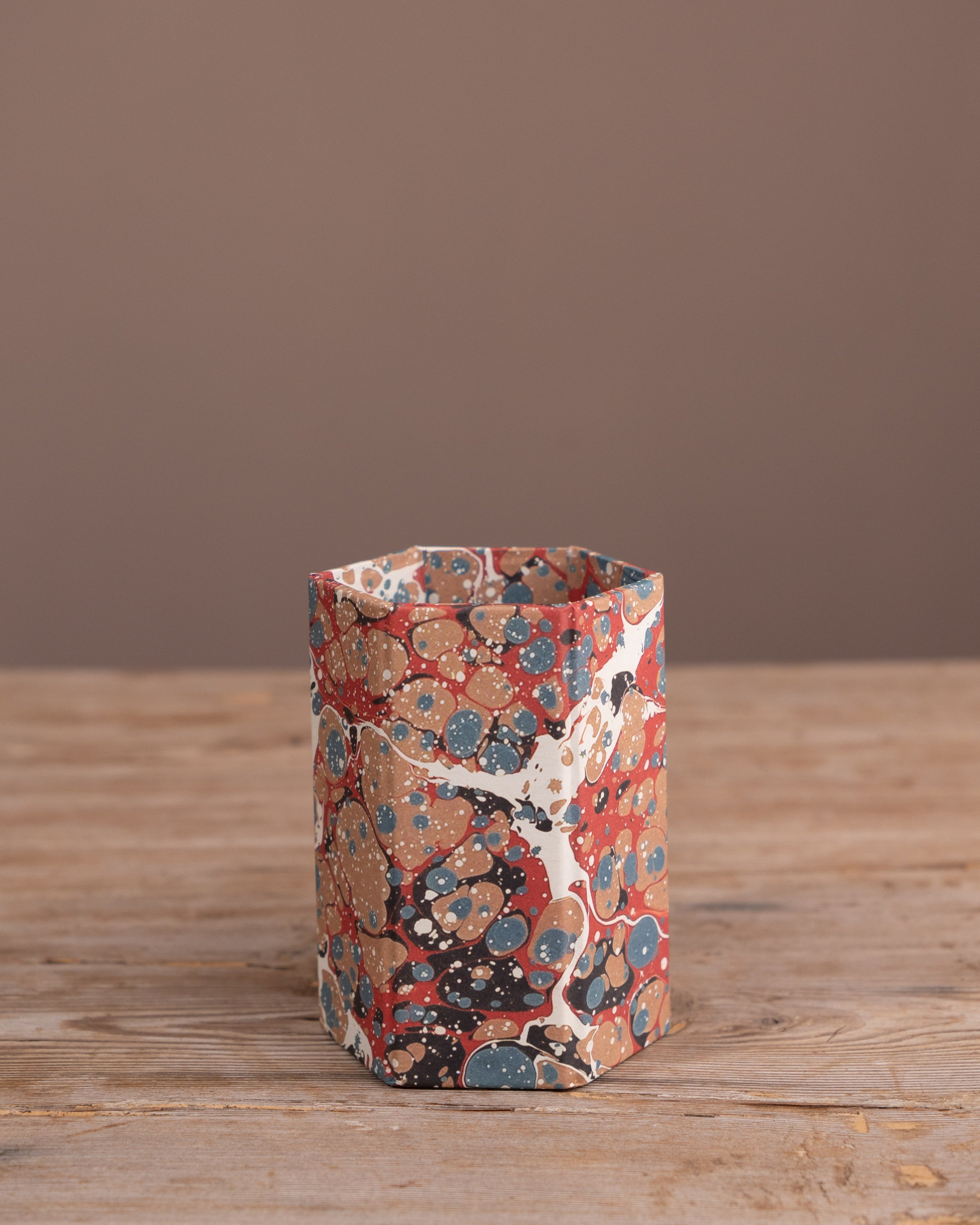 Marbled hexagonal pen pot on a wooden surface with a brown background