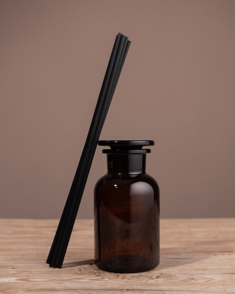 Brown diffuser bottle with black reeds on a wooden surface and brown background