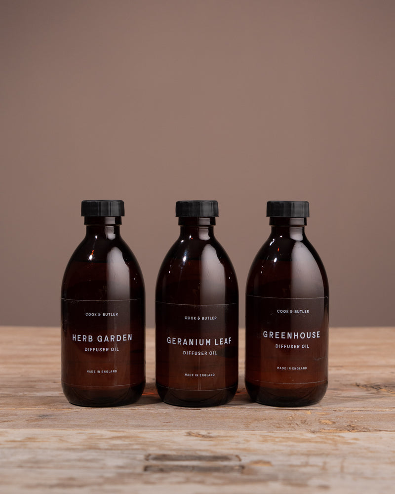 Three diffuser oil bottles from Caudle & Co. on a wooden surface with a brown background