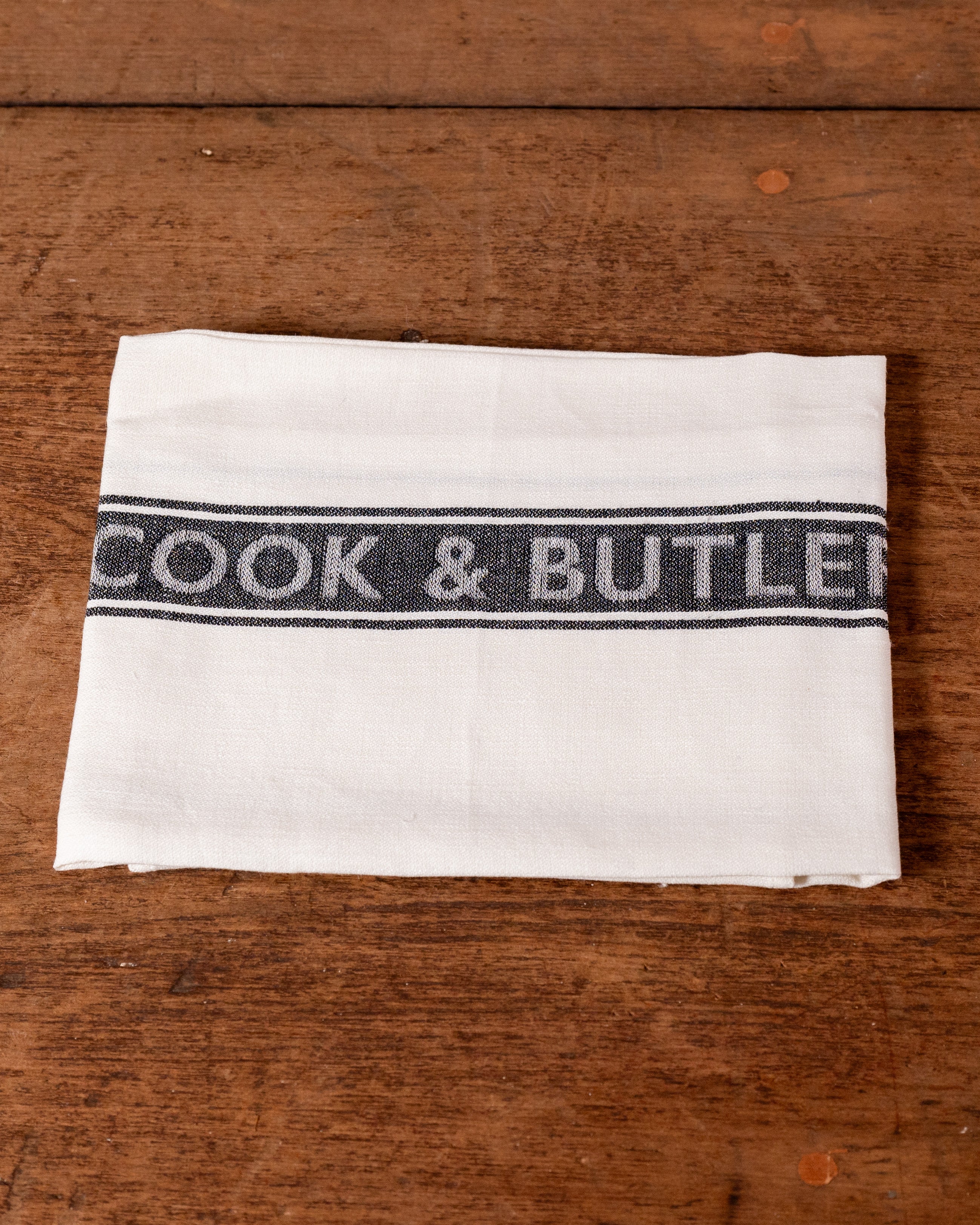White towel with 'Cook & Butler' branding on a wooden surface