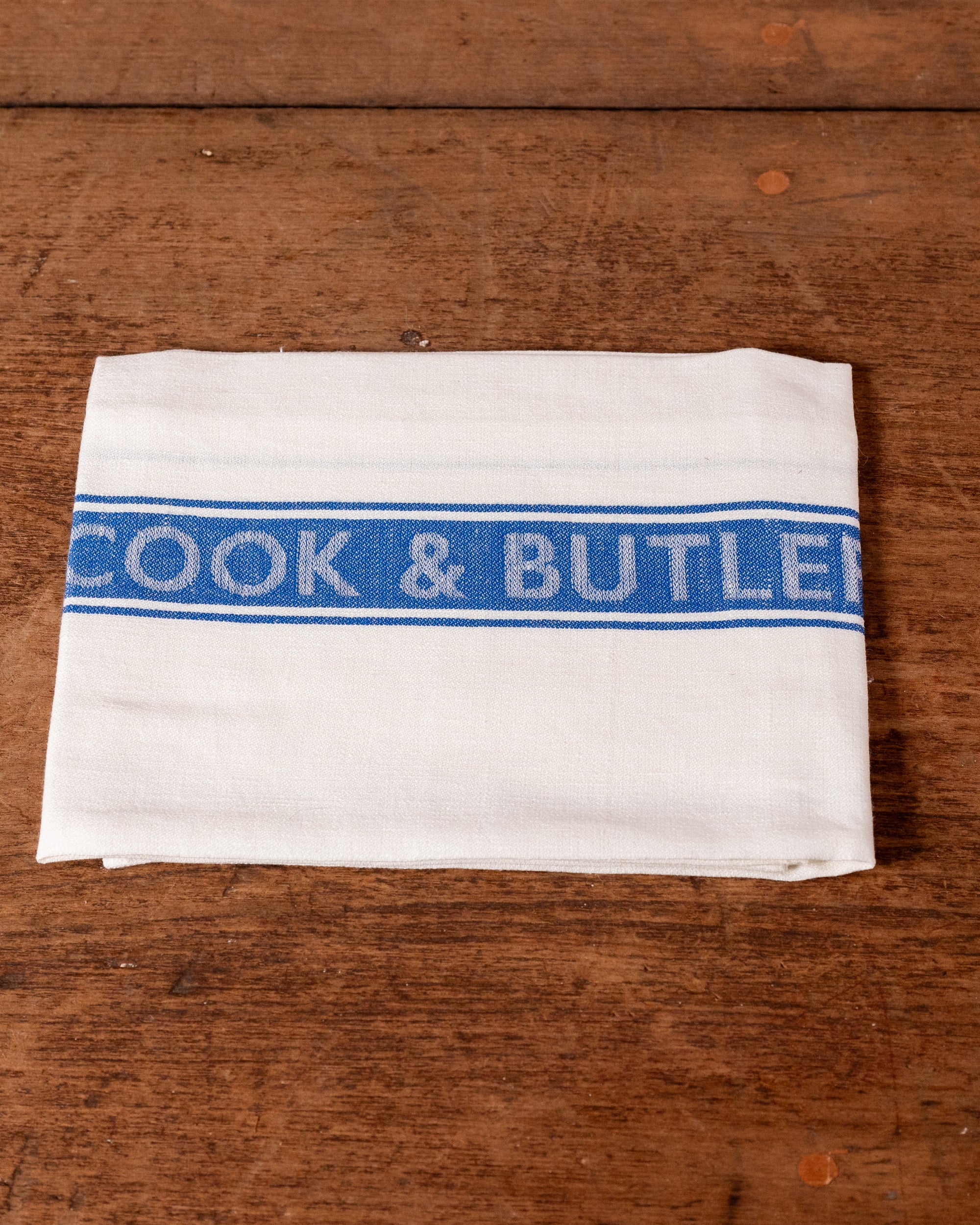 White towel with blue 'Cook & Butler' stripe on a wooden surface