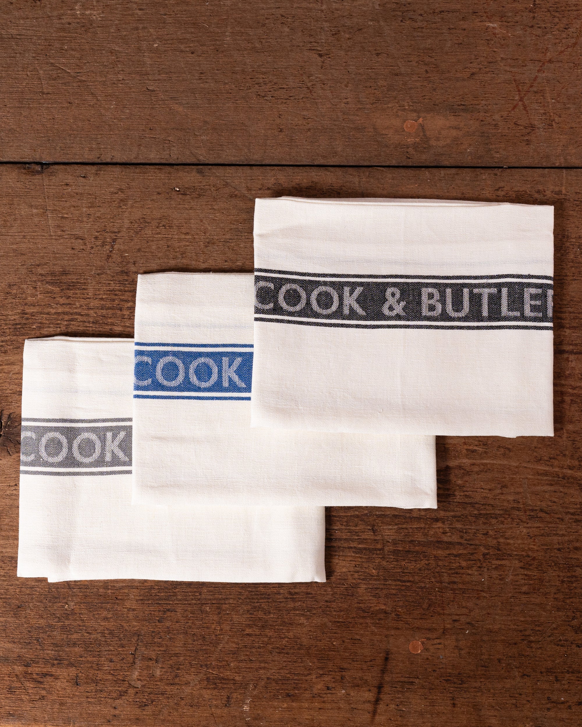 Two white towels with 'Cook & Butler' branding on a wooden surface