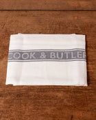 White towel with 'Cook & Butler' branding on a wooden surface