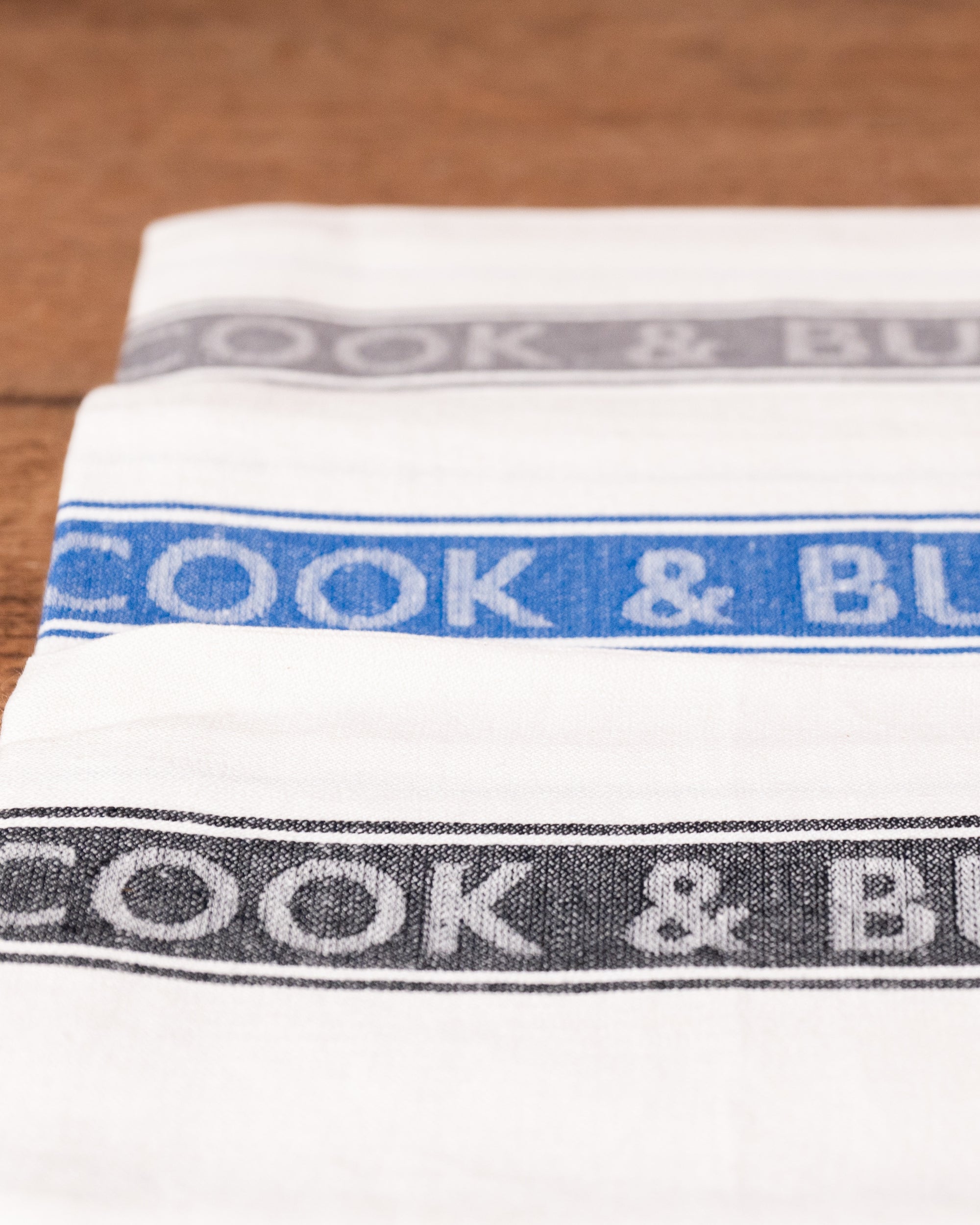 Stack of white tea towels with 'Cook & Butler' branding on a wooden surface