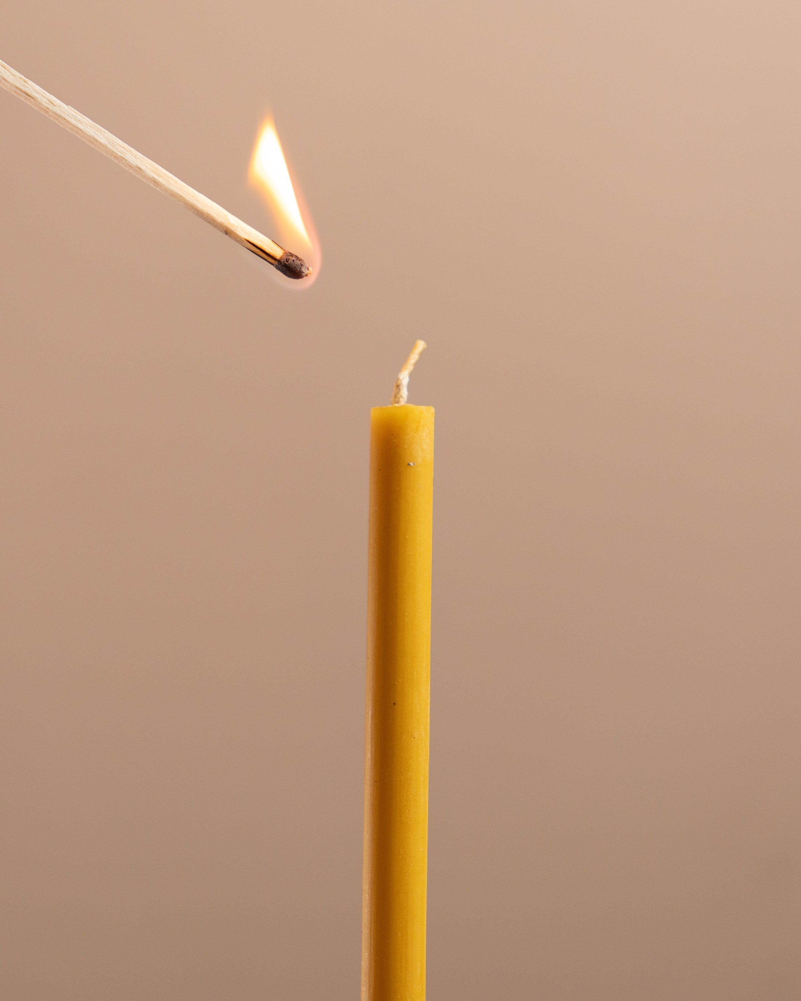 Match lighting a yellow candle against a beige background