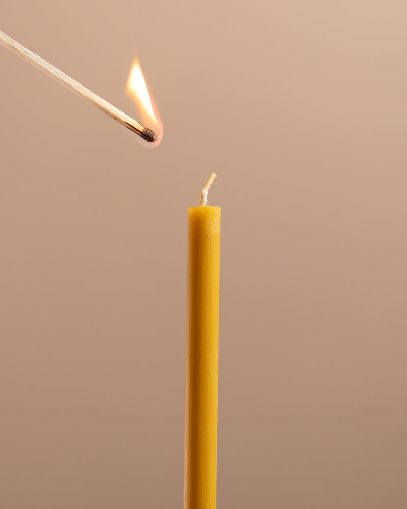 Match lighting a yellow candle against a beige background