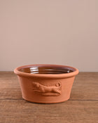 Terracotta pet bowl with dog design on a wooden surface