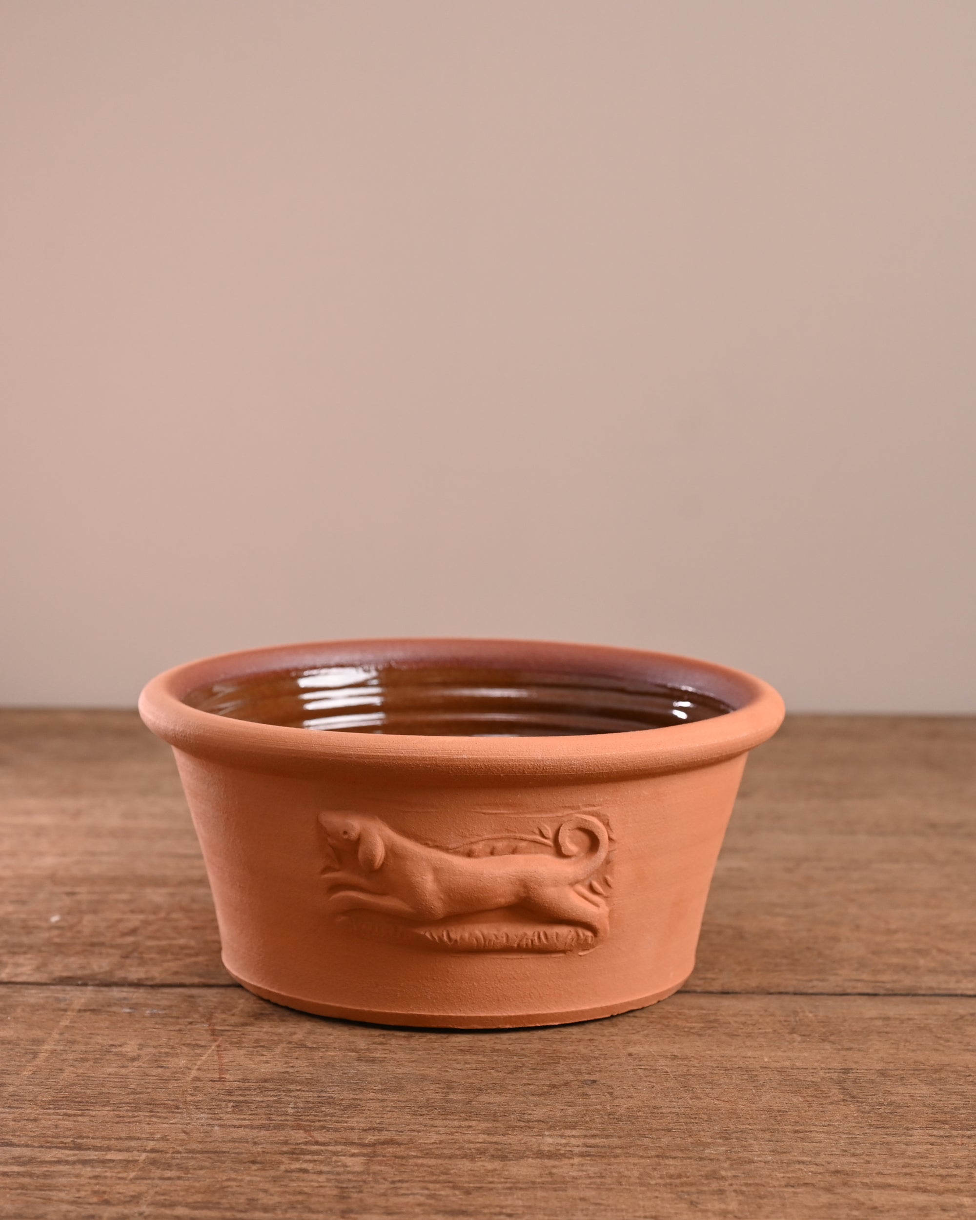 Terracotta pet bowl with dog design on a wooden surface