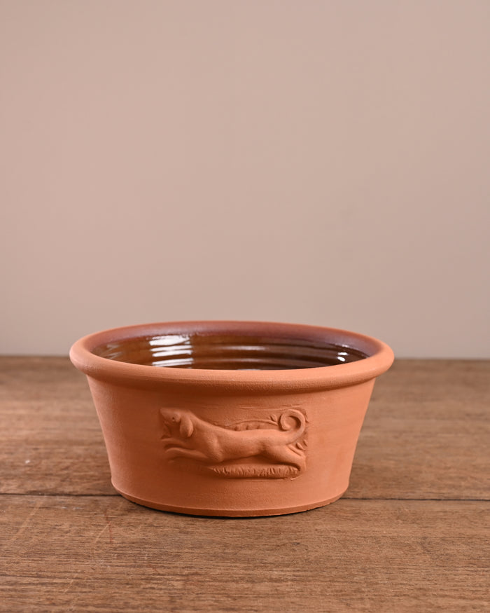 Terracotta pet bowl with dog design on a wooden surface