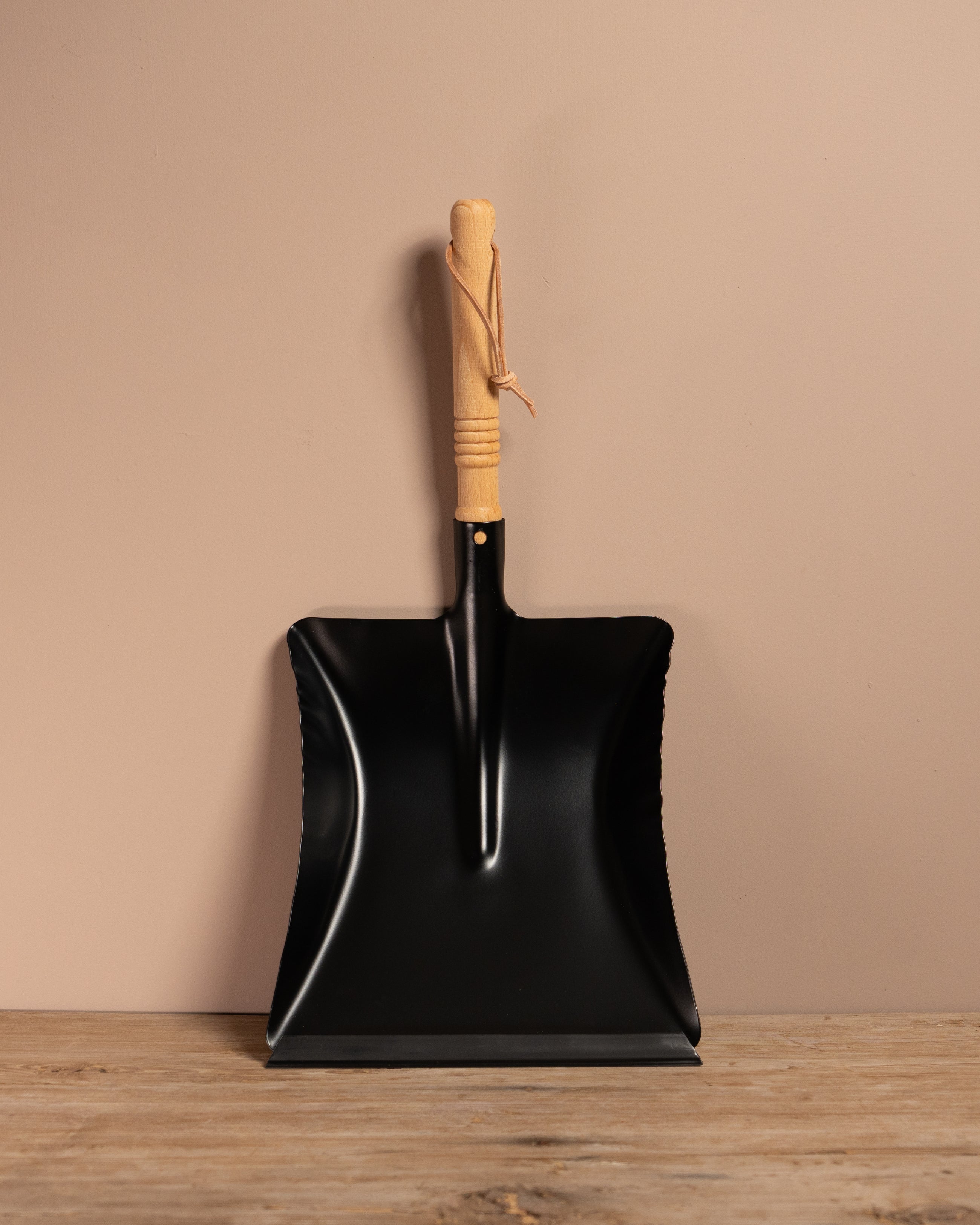Black metal shovel with wooden handle on a wooden surface and beige wall background
