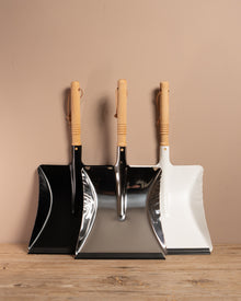 Set of three dustpans with wooden handles on a wooden surface against a beige wall.