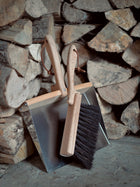 Metal dustpan and wooden brush against some logs