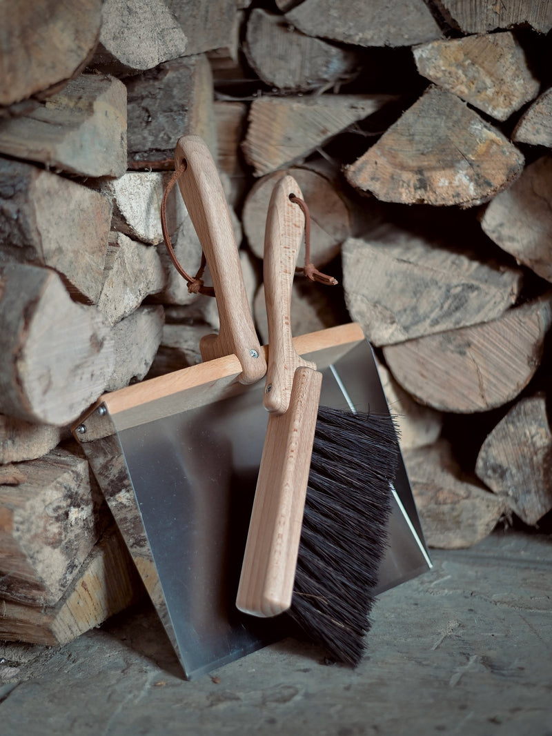 Metal dustpan and wooden brush against some logs
