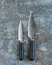 Two knives with ebony handles on a textured gray surface