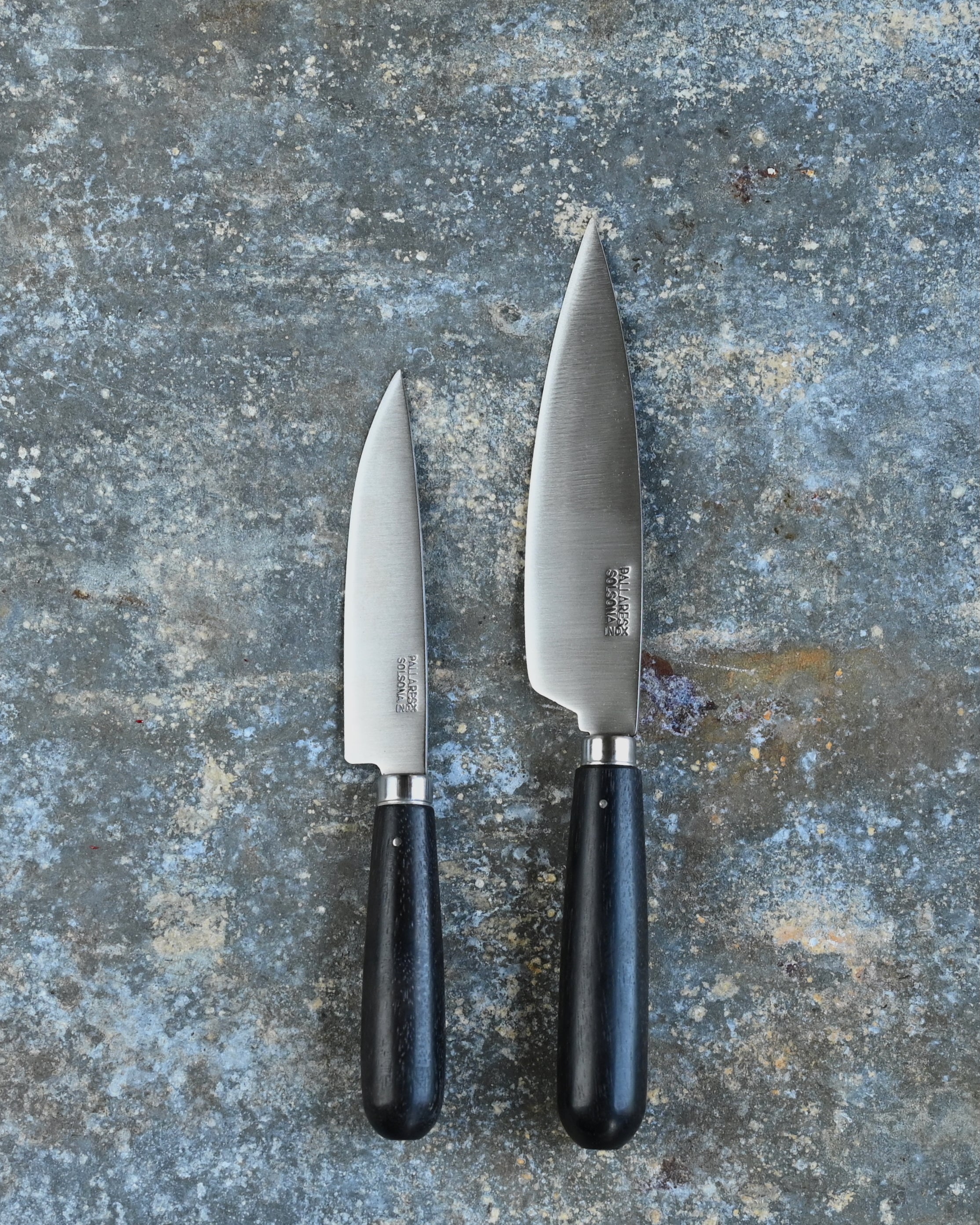 Two knives with ebony handles on a textured gray surface