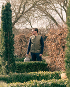 Man wearing a green field vest standing in a garden with trees and shrubs