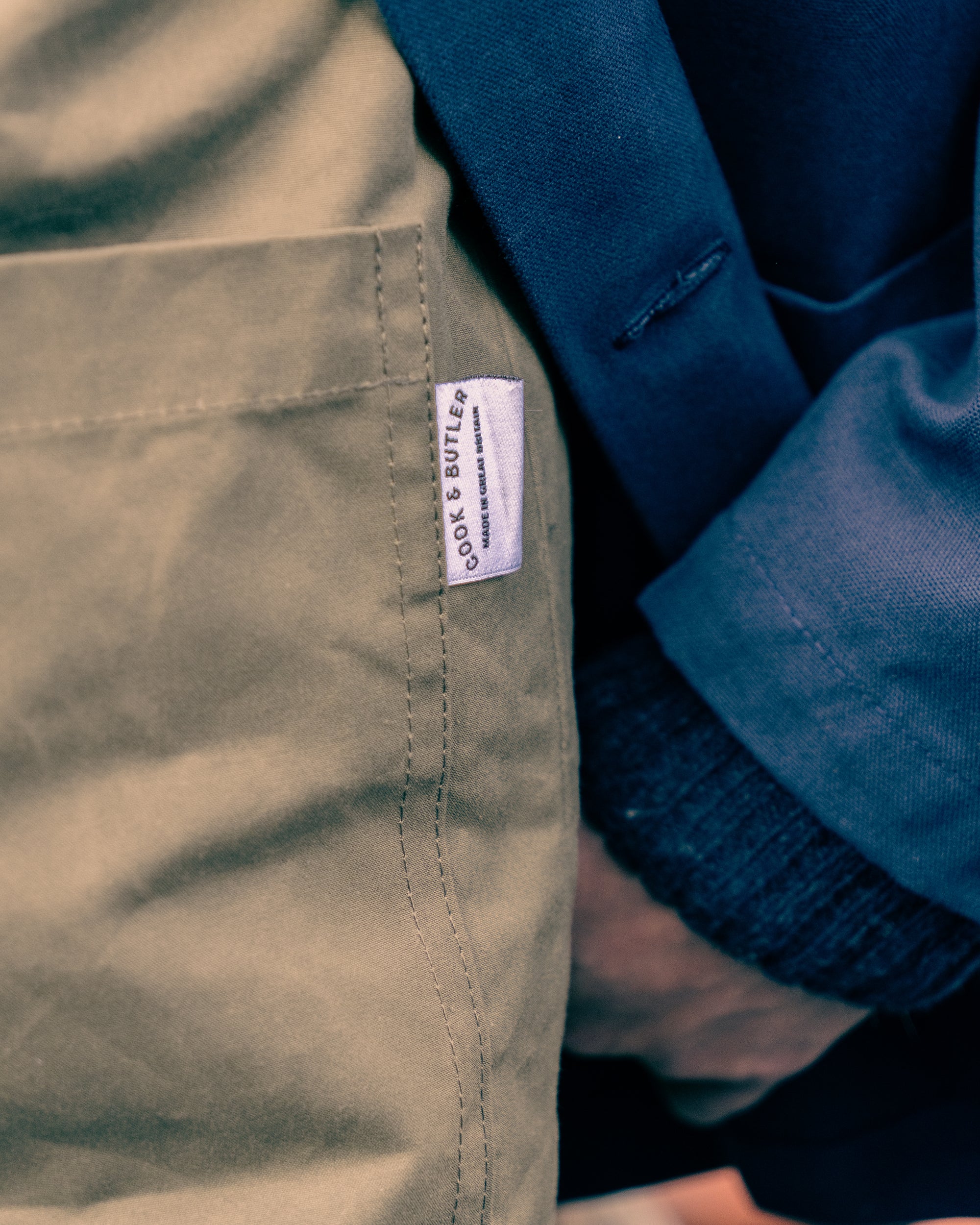Close-up of a label saying "Cook & Butler" on a green work vest with a blue garment in the background