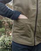 Person wearing a green work vest with a blurred natural background