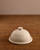Speckled ceramic cloche butter dish on a wooden surface