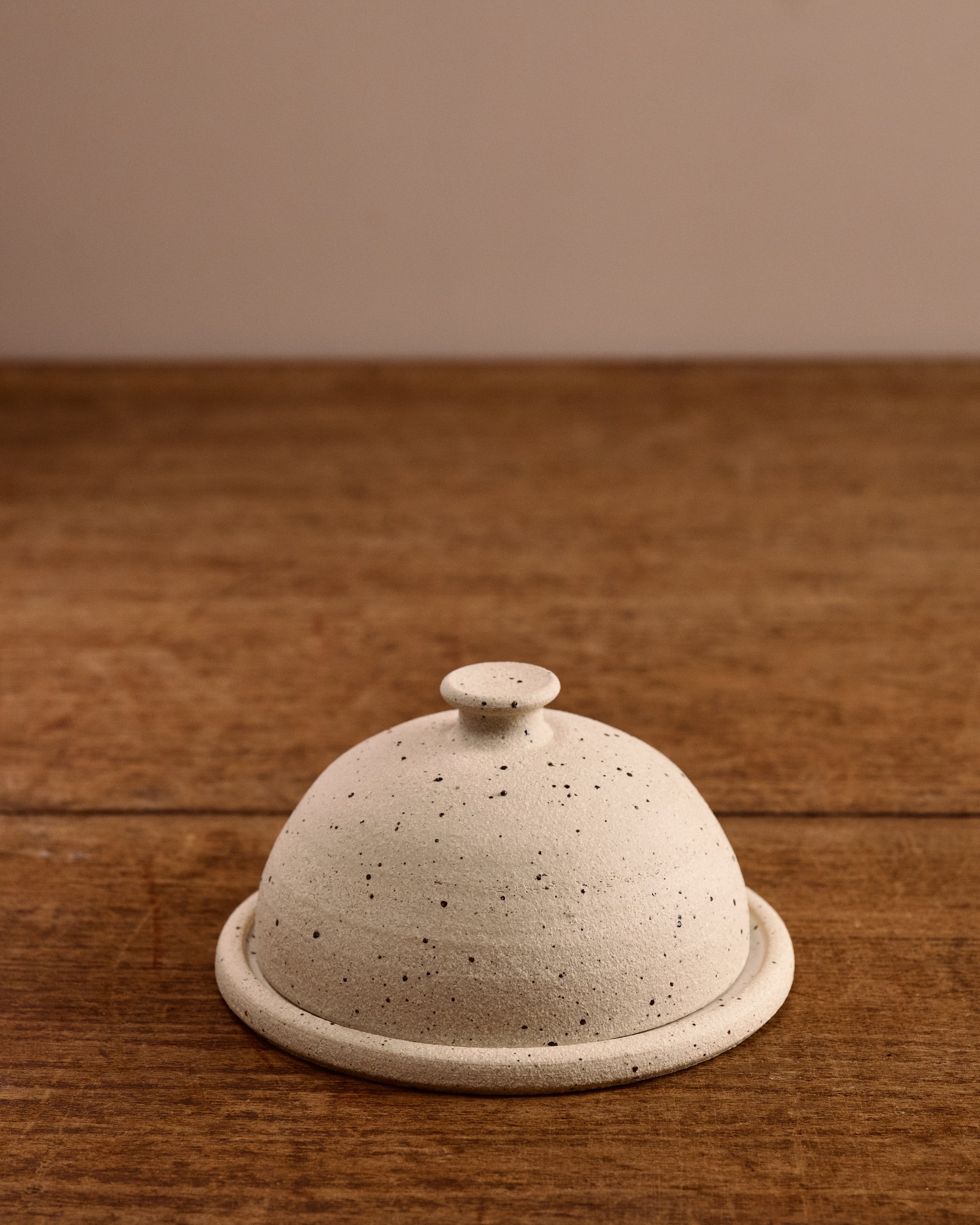 Speckled ceramic cloche butter dish on a wooden surface
