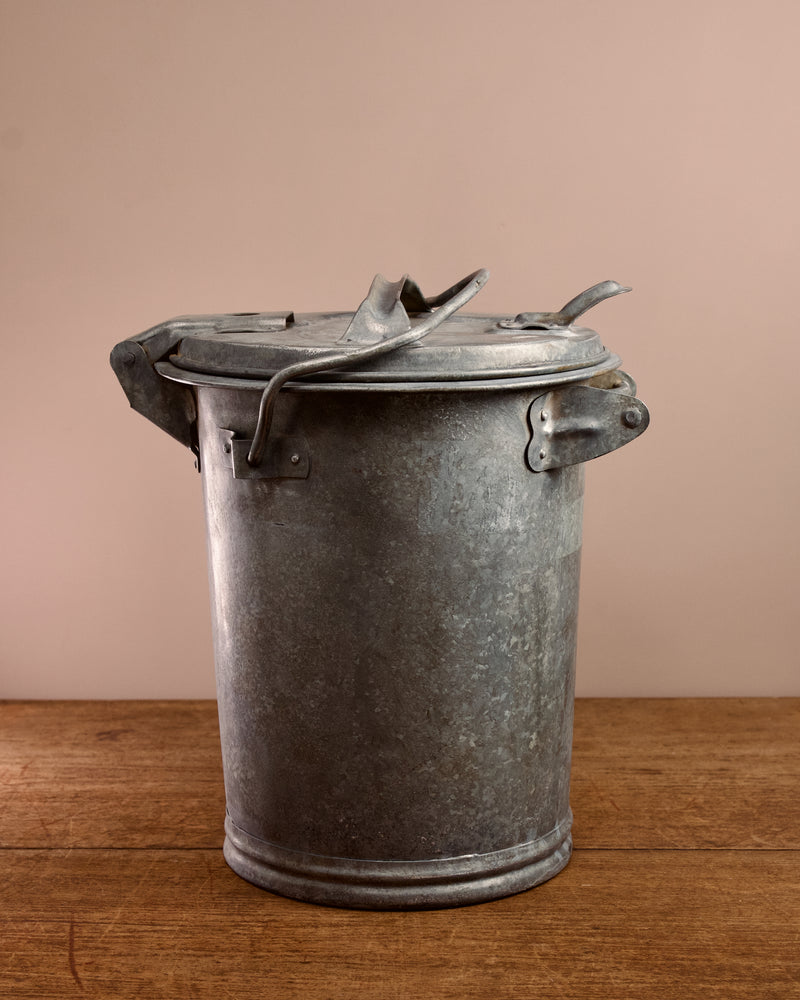 Vintage-style metal ash can on a wooden surface with a beige background