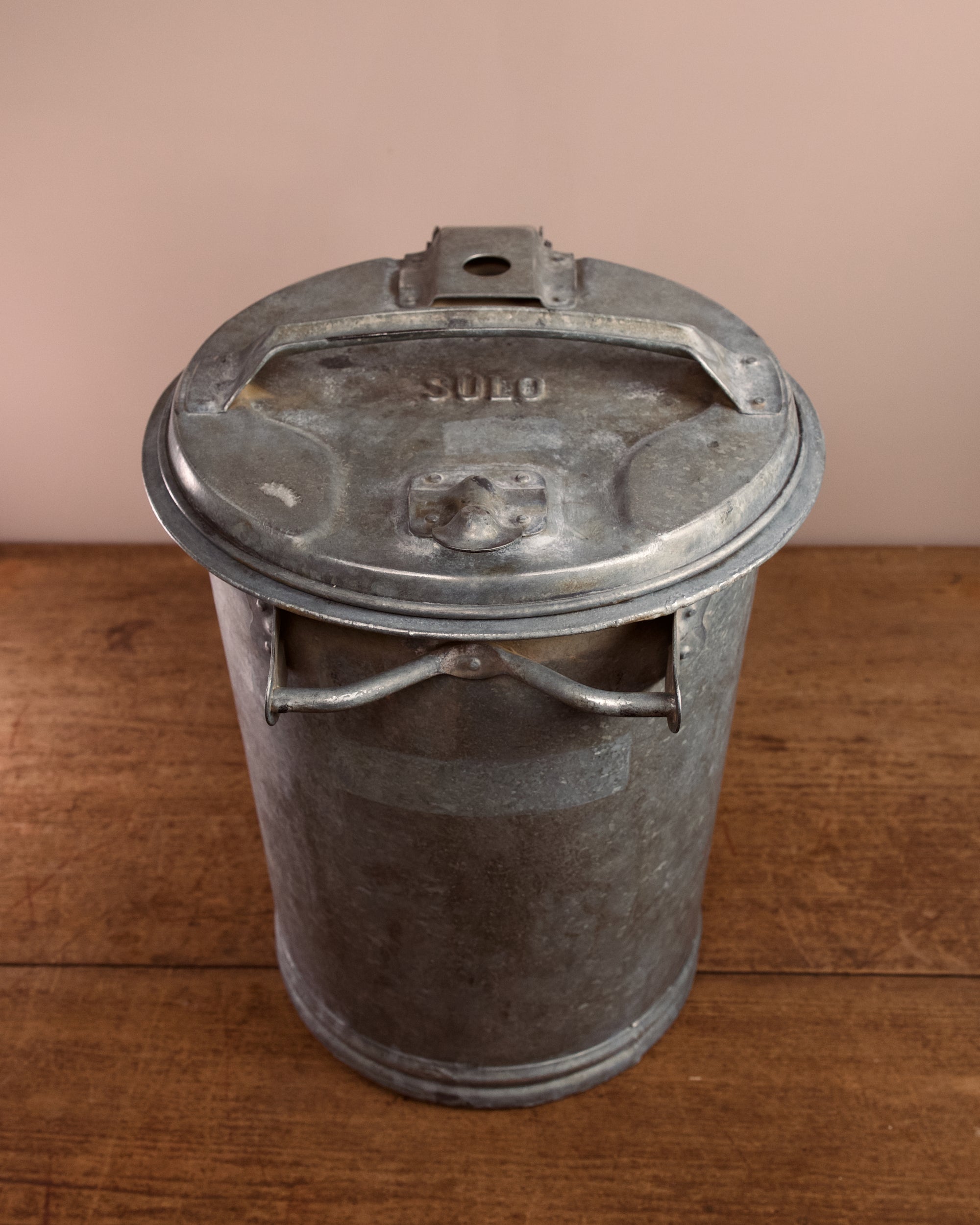 Vintage-style metal ash can on a wooden surface with a beige background