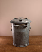 Vintage-style metal ash can on a wooden surface with a beige background