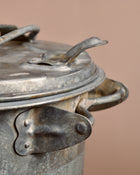 Vintage-style metal ash can on a wooden surface with a beige background