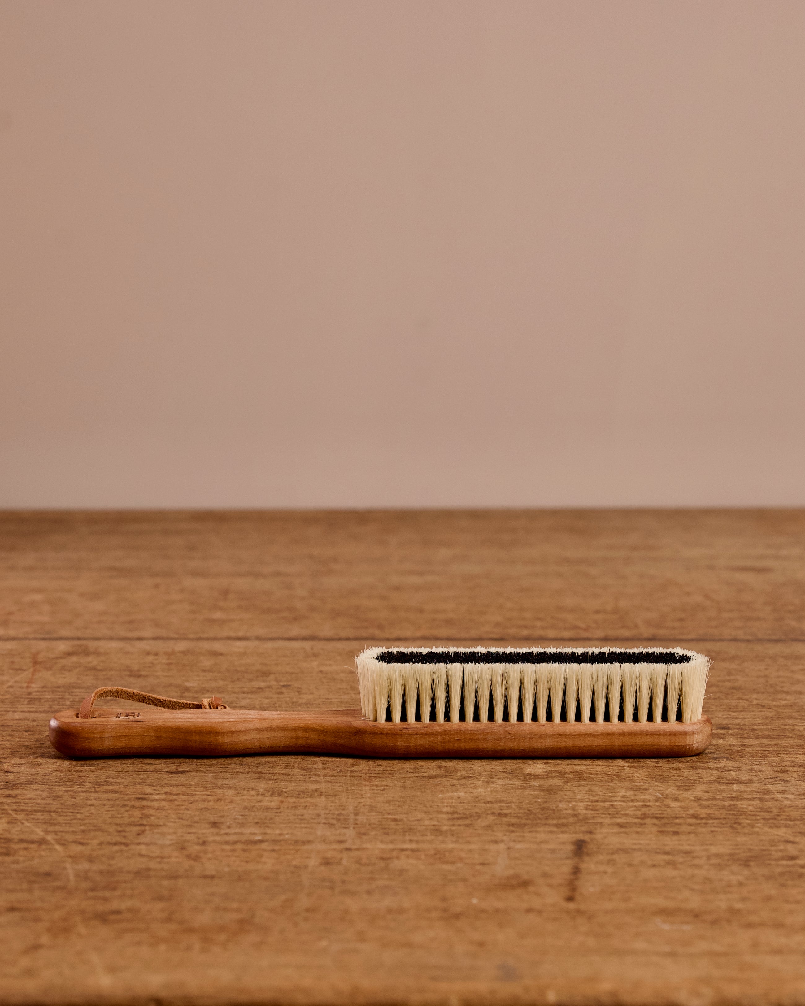 Handheld brush with wooden handle and bristle head on a wooden surface