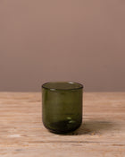 Green glass tumbler on a wooden surface with a brown background