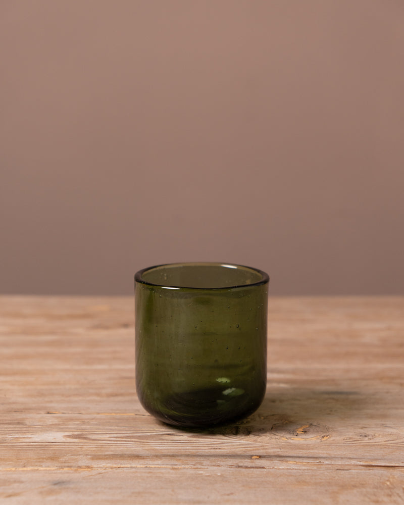 Green glass tumbler on a wooden surface with a brown background
