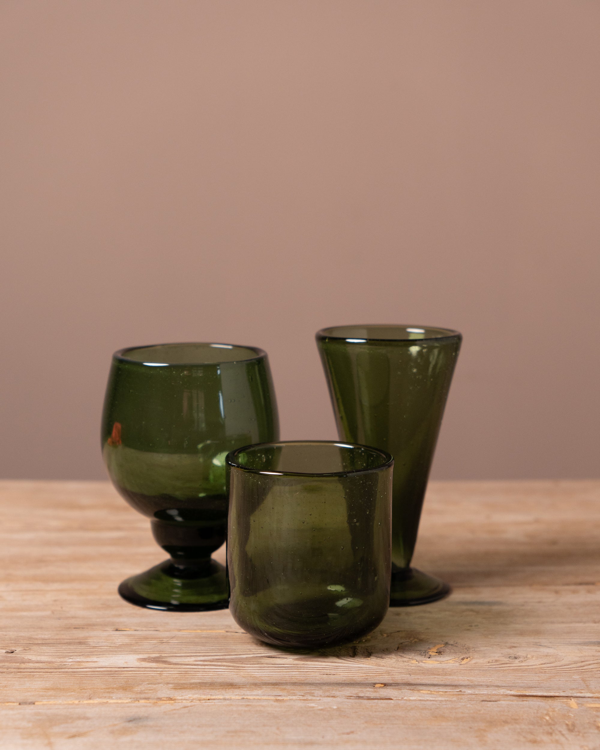 Three green glass tumblers on a wooden surface with a beige background