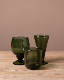 Three green glass tumblers on a wooden surface with a beige background