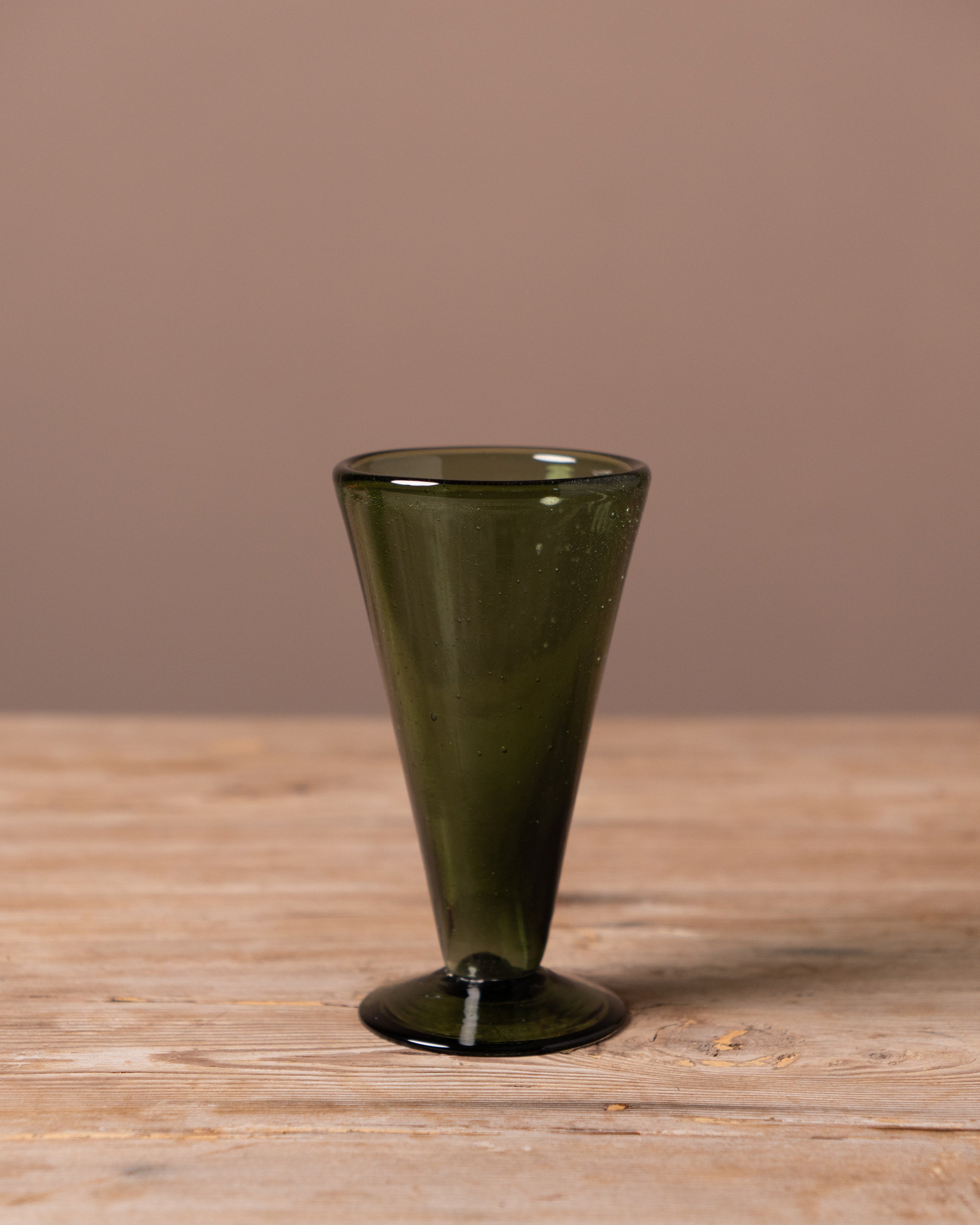 Green glass drinking vessel on a wooden surface with a brown background