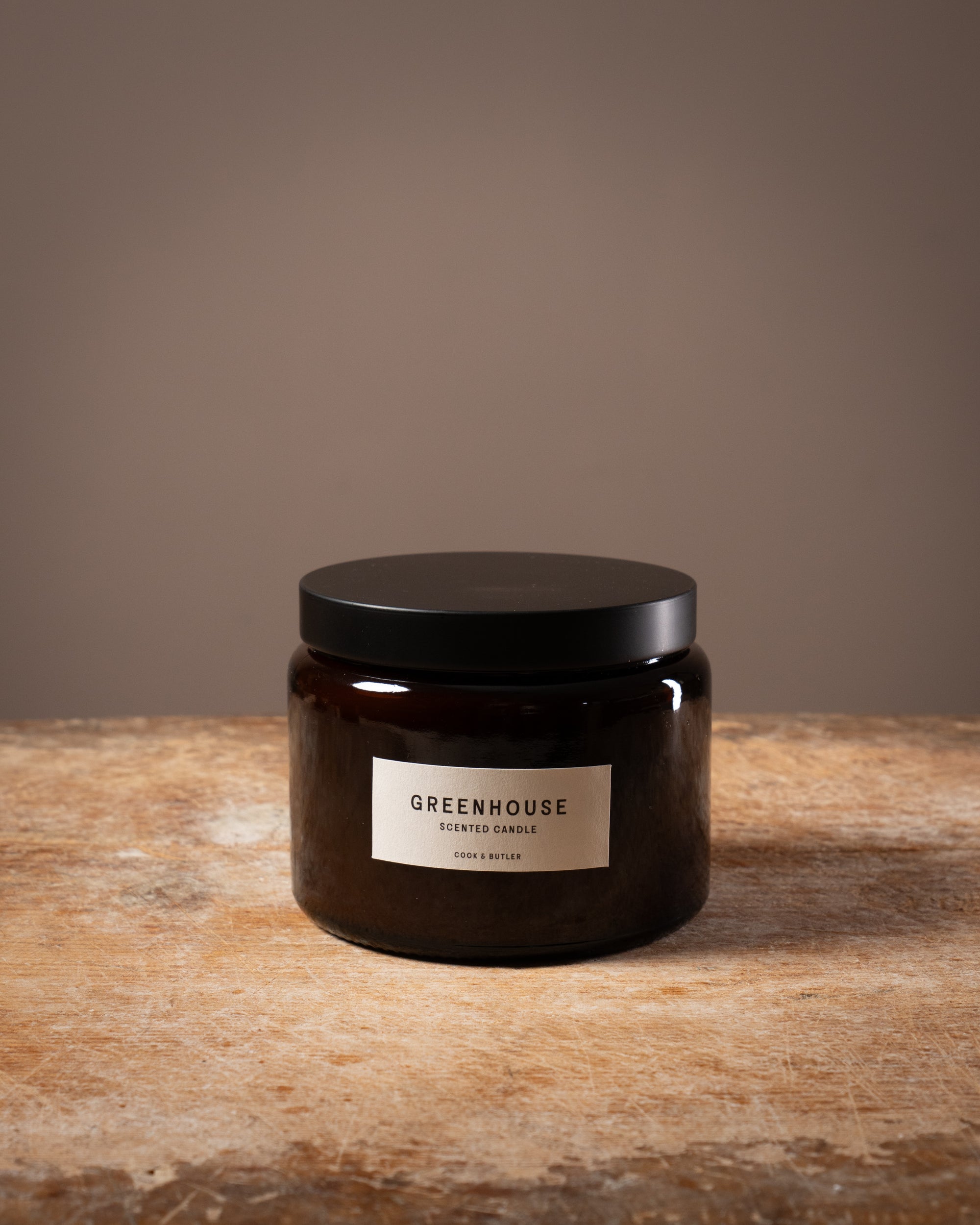 Cook and Butler scented candle on a wooden worktop with a label saying "greenhouse"