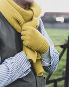 Person wearing a yellow knitted scarf and gloves with a blurred outdoor background