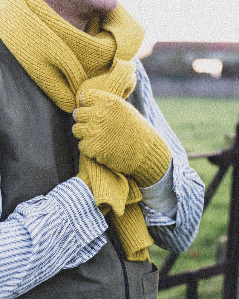 Person wearing a yellow knitted scarf and gloves with a blurred outdoor background