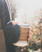 Hand holding a steaming mug outdoors with a blurred natural background