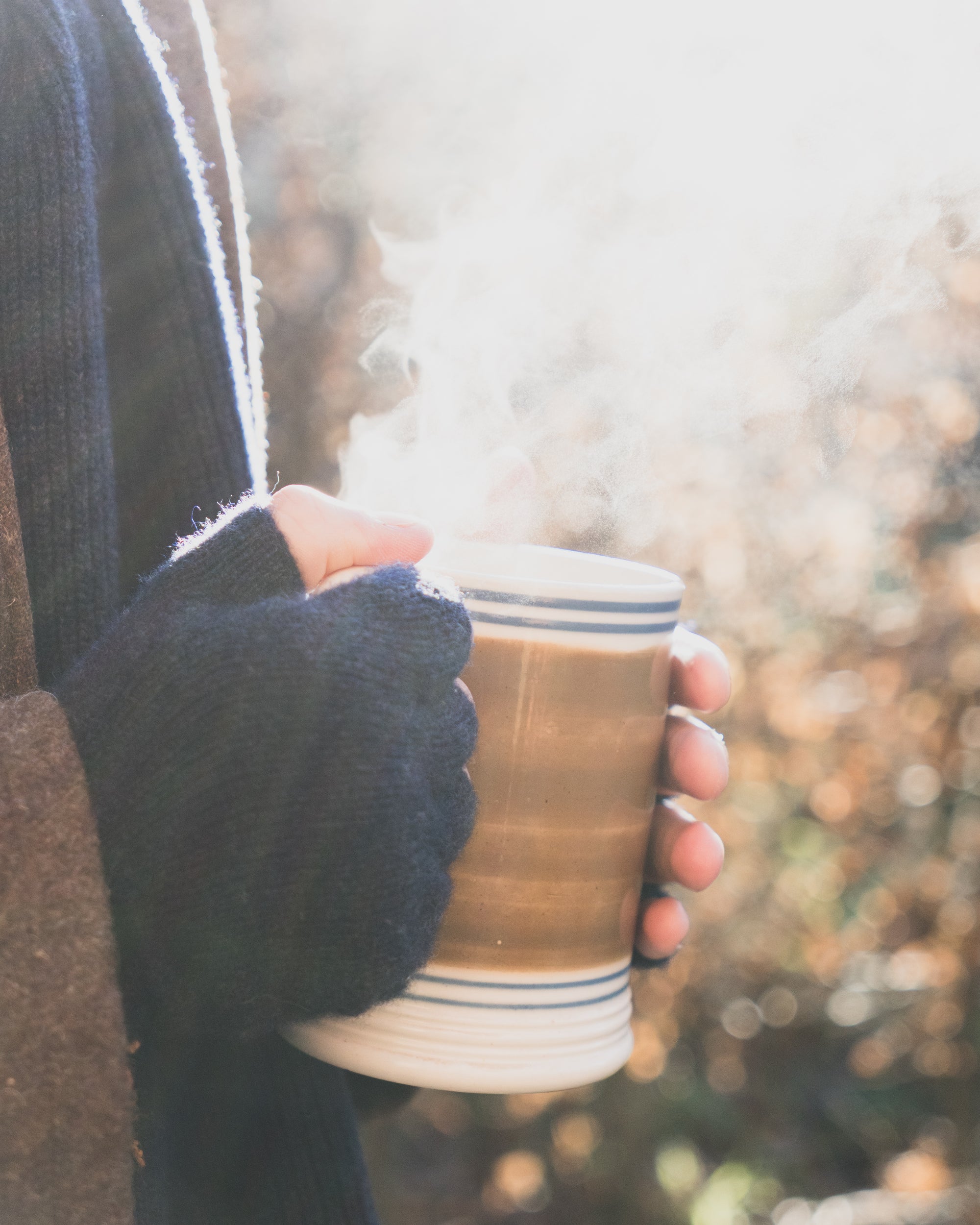 Hand holding a steaming mug outdoors with a blurred natural background
