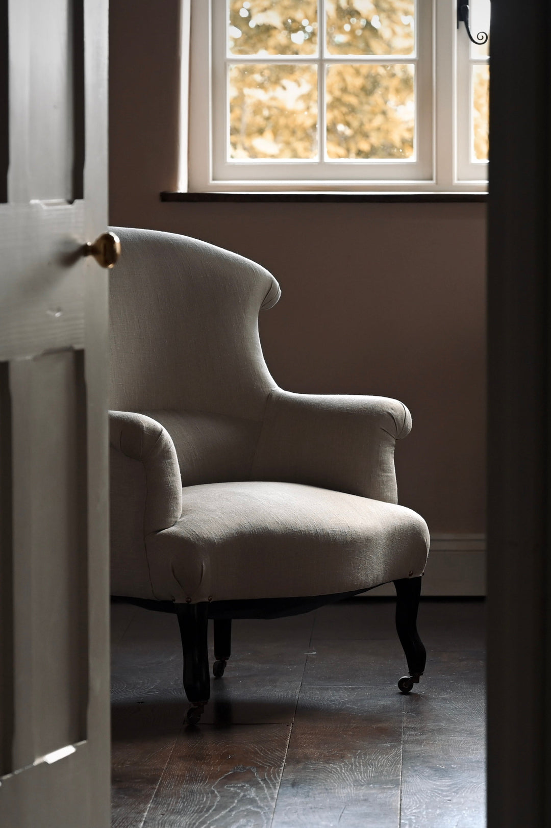 Linen-covered chair in a sitting room with a window and wooden floor